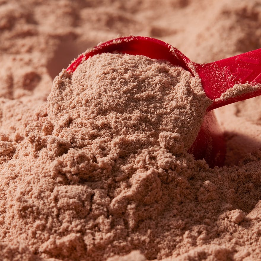 A red scooper in a pile of chocolate protein powder.