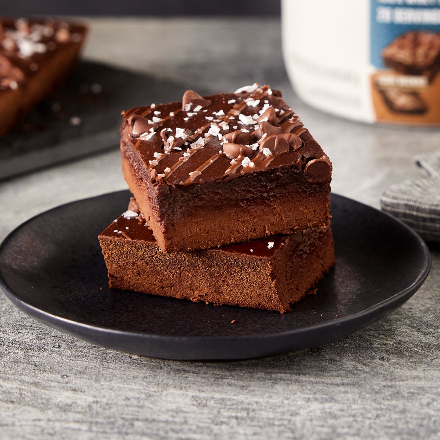 Protein Packed Brownies on a plate with a tub of Dymatize ISO100 Fudge Brownie Protein Powder